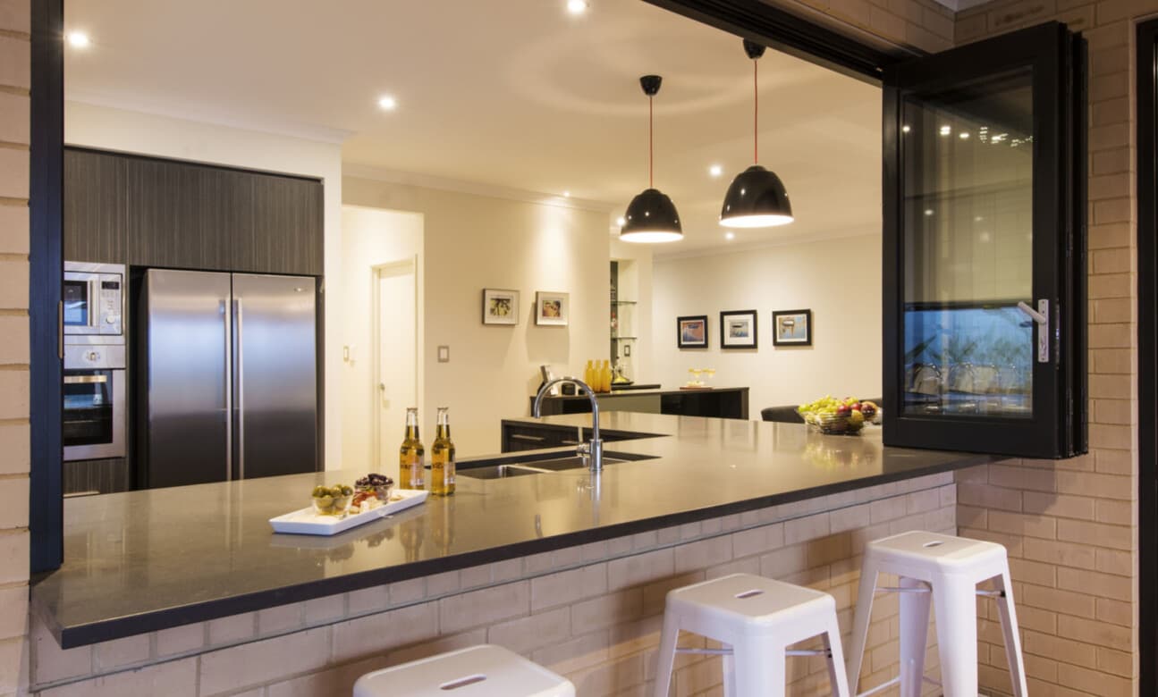 Modern kitchen with a grey breakfast bar, white stools, and an open bi-fold window.
