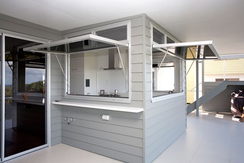 Two large awning windows open upwards on a grey exterior wall, creating an outdoor bar.